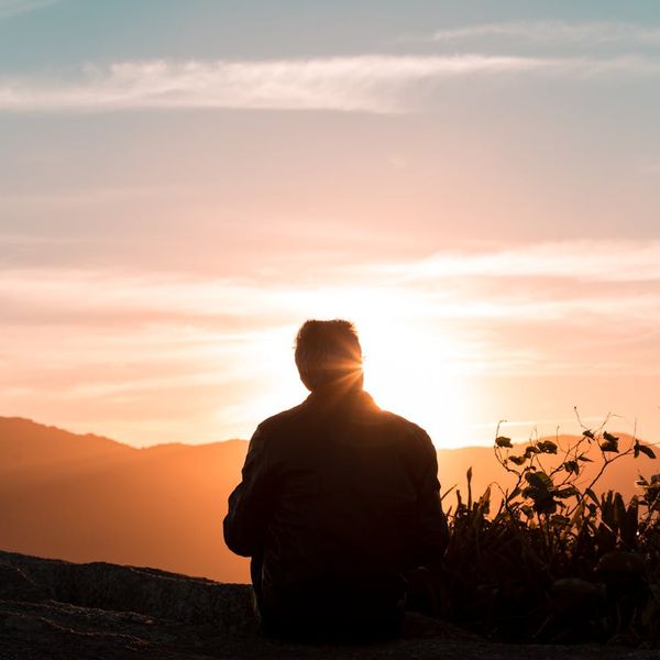 Person meditating peacefully outdoors during sunset with a beautiful landscape.